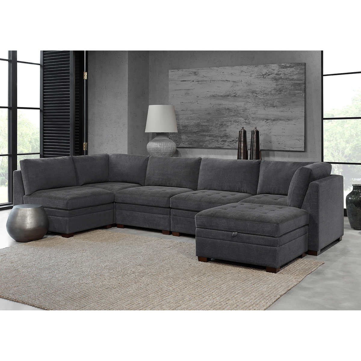 A modern gray fabric sectional sofa with a storage ottoman in a living room.