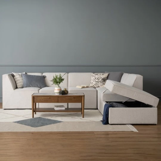 Beige L-shaped modular sofa with storage ottoman in a living room.